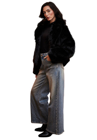 Woman in a black fur coat and jeans standing in front of a red sofa and painting.