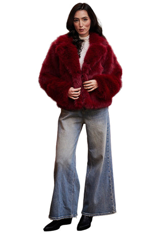 Woman wearing a red fur coat and jeans standing in front of a red sofa and painting.
