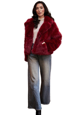 Woman wearing a red fur coat in a room with a red sofa and a large painting in the background.