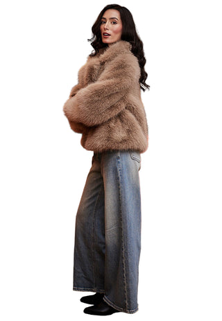 Woman wearing a fur coat and jeans standing in front of a red sofa and painting.