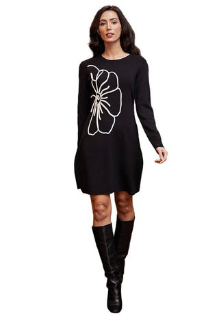 Woman wearing a black dress with a white floral design in an indoor setting.