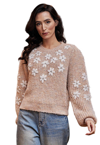 Woman wearing a beige sweater with white floral patterns in a decorative indoor setting.