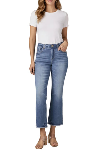 A model wearing a white short-sleeve crewneck top and high-waisted, cropped blue denim jeans with a subtle flare at the hem, paired with beige heeled sandals, set against a solid warm gray studio background.