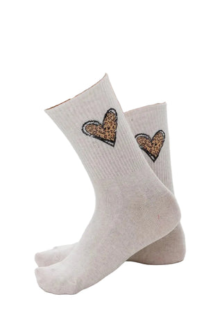 A pair of off-white crew socks worn on feet, featuring a leopard-print heart design outlined in black on the upper calf.
