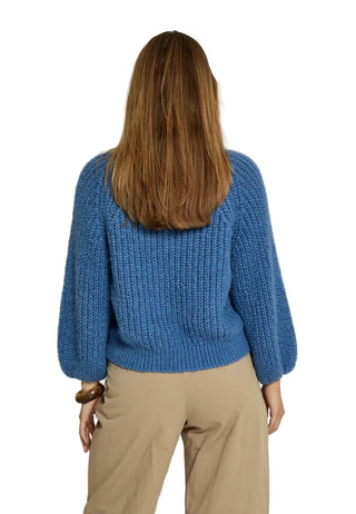 Person wearing a blue knitted sweater and beige pants against a white background
