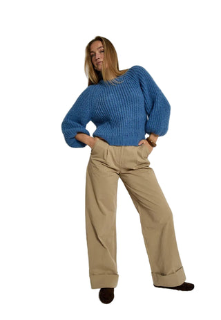 Person wearing a blue sweater and beige pants on a white background