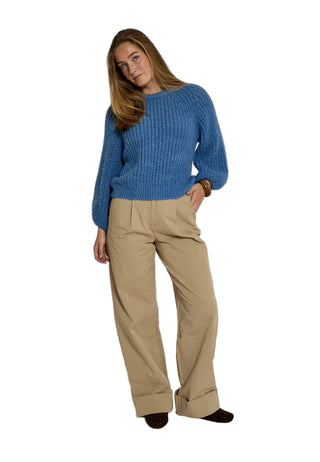 Woman wearing a blue sweater and beige pants on a white background