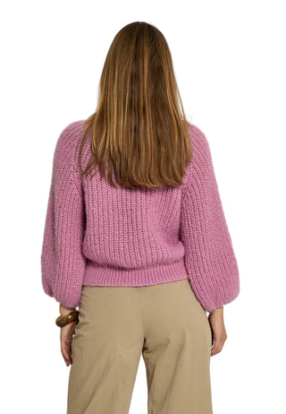 Person wearing a pink knitted sweater and beige pants against a white background