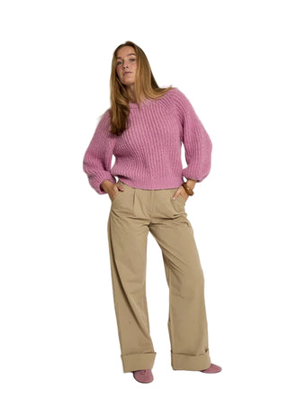 Woman wearing a pink sweater and beige pants on a white background