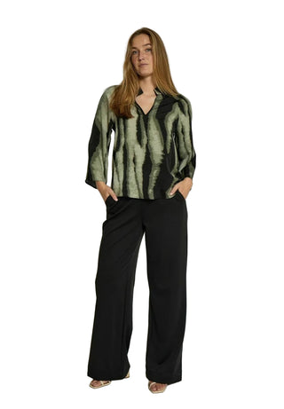 Woman wearing a green and black patterned top with black pants on a white background