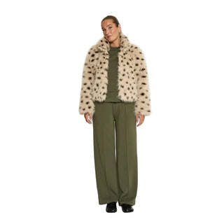 Person wearing a beige faux fur coat with black spots, green sweater, and olive green pants on a white background
