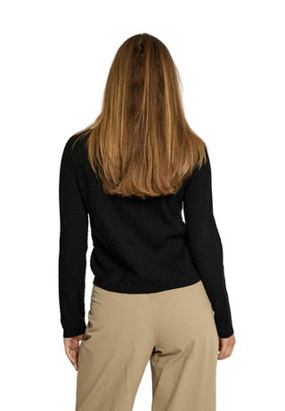 Person wearing a black long-sleeve top and beige pants against a white background