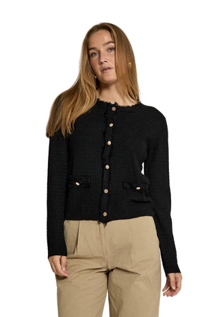 Woman wearing a black cardigan and beige pants against a white background