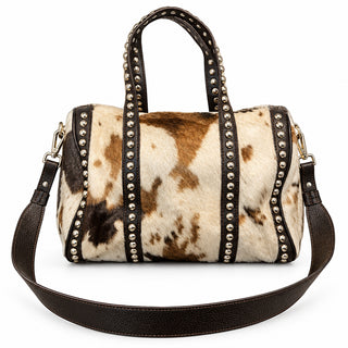 A cowhide handbag with black faux-leather trim and gold-tone studs, displayed on a gray countertop.
