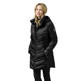 A woman wearing a black mid-length puffer coat with a high collar and front zipper, standing against a plain light gray studio background.