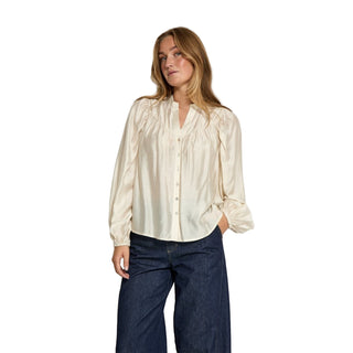 Woman wearing a cream blouse and dark jeans against a white background
