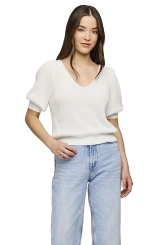 Woman wearing a white blouse and light blue jeans against a plain background
