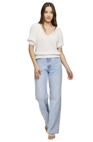Woman wearing a white top and light blue jeans on a plain background