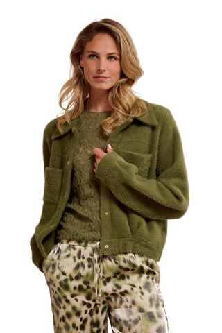 Woman wearing a green knitted cardigan over a green sweater with leopard print pants on a beige background