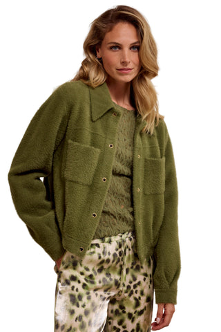 Woman wearing a green cardigan over a patterned top with a neutral background