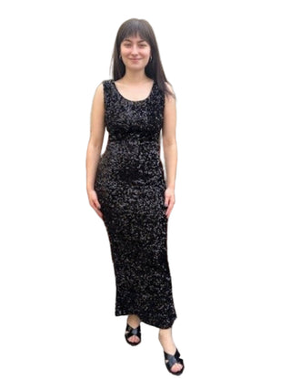 Woman wearing a black sequin dress standing against a brick wall.