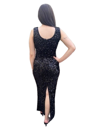 Person wearing a black sequin dress with a high slit, standing against a brick wall.