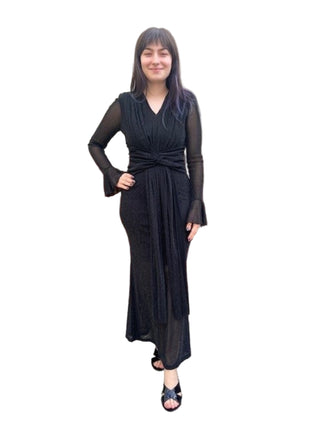 Woman wearing a black dress standing against a brick wall.