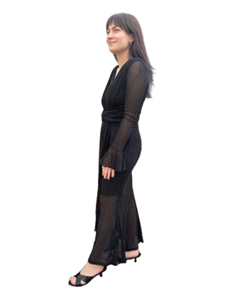 Woman wearing a black dress standing against a brick wall.