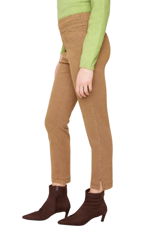 A model shown from the waist down wearing slim-fit brown ankle-length jeans, a light green knit sweater, and dark brown pointed-toe heeled ankle boots, photographed against a light gray studio background.