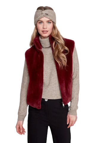 Woman wearing a red fur vest, beige sweater, black pants, and headband on a white background