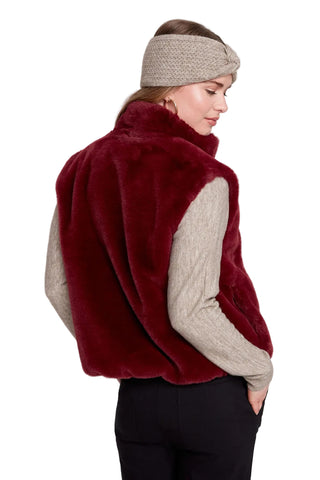 Woman wearing a red fur vest over a beige sweater on a white background