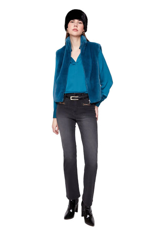 A model stands against a light gray studio background wearing a teal velvet jacket over a matching teal top, dark gray skinny jeans, black ankle boots, and a black hat.