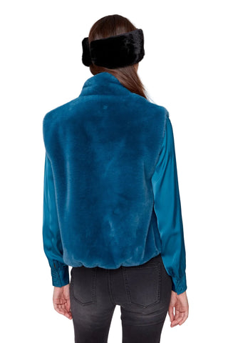 A model shown from the back wearing a teal blue velvet cropped jacket over a satin long-sleeve top, paired with a black faux-fur headband and dark gray jeans, against a plain light gray background.