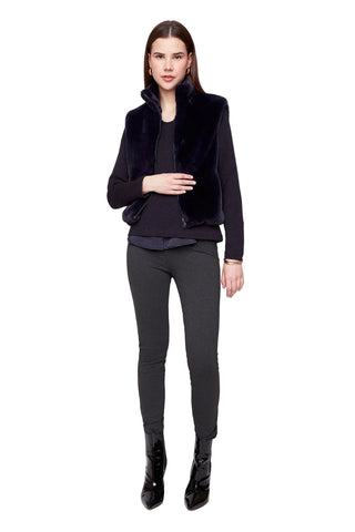 Woman wearing a black fur vest over a dark top and gray pants on a white background