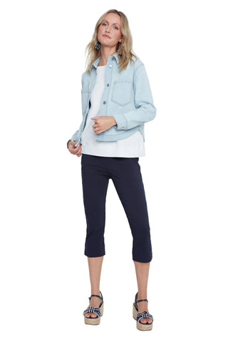 Woman wearing a light blue denim jacket, white shirt, and navy capri pants on a white background