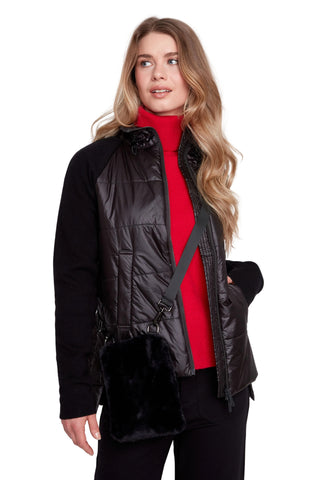 A woman modeling a black quilted puffer vest with a black faux-fur trim over a bright red turtleneck sweater and black pants, against a light gray studio background.