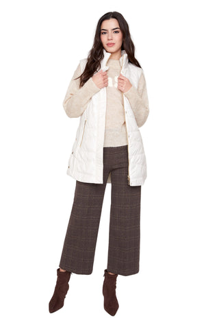 Woman wearing a beige puffer vest over a white shirt with plaid pants on a white background