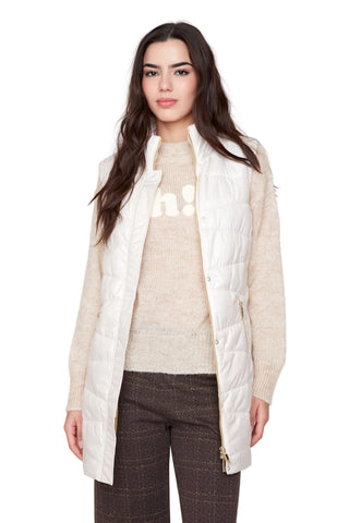 Woman wearing a white puffer vest over a beige sweater and plaid pants on a white background