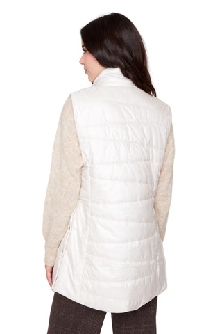 Woman wearing a white puffer vest over a beige sweater on a white background