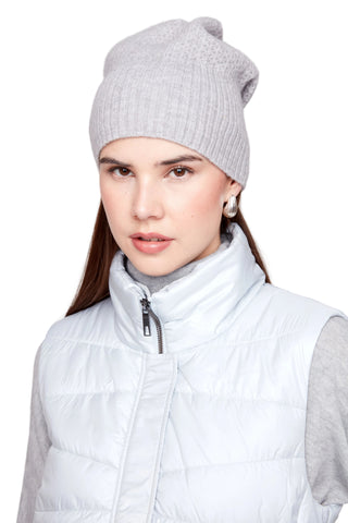 Woman wearing a gray knit beanie and light gray puffer vest on a white background