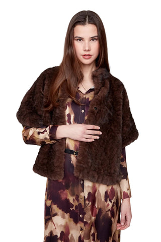 Woman wearing a brown fur coat over a patterned dress on a white background