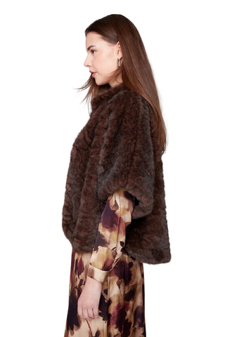 Woman wearing a brown fur coat over a patterned dress on a white background