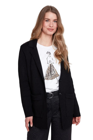 Woman wearing a black blazer over a white graphic t-shirt on a plain background