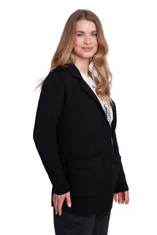 Woman wearing a black blazer over a white top with a pattern on a plain background