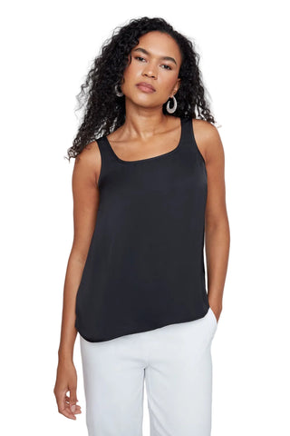 Woman wearing a black sleeveless top and white pants against a plain background