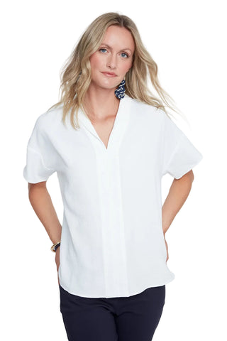 Woman wearing a white blouse and dark pants against a plain background