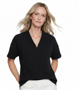 A woman modeling a black short-sleeve V-neck scrub top against a light gray studio background.