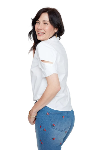 Woman wearing a white shirt and blue jeans with red embellishments on a light gray background