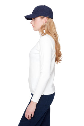 Woman wearing a navy cap and white sweater against a plain background