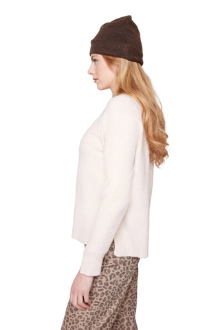 Woman wearing a white sweater and leopard print pants with a brown beanie on a light gray background